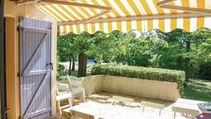 Een terras buiten met een tafel en stoelen, een overdekte zithoek en een uitzicht op een tuin met bomen en een zwembad op de achtergrond.