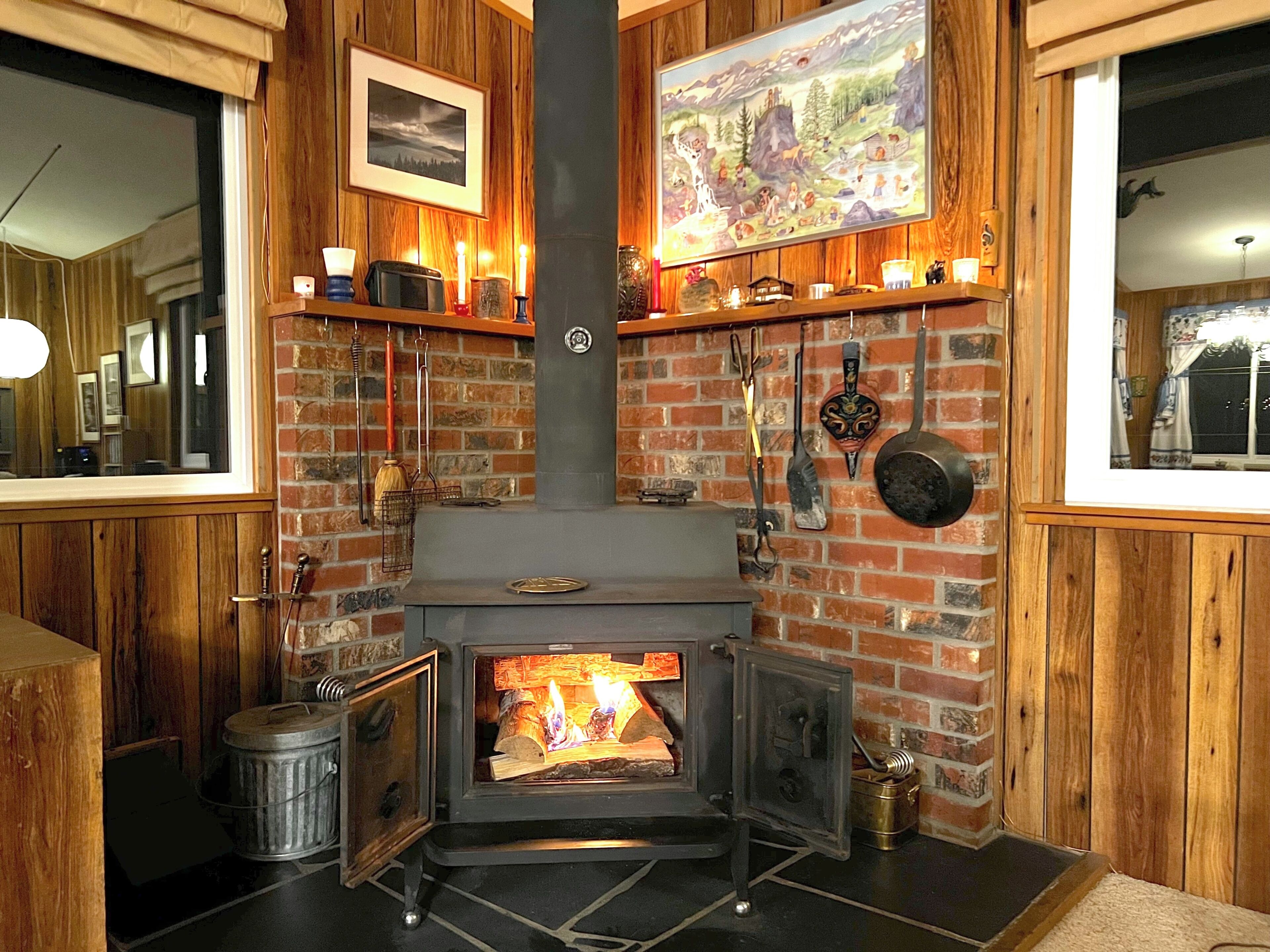 Un poêle à bois avec un feu, un tableau encadré au-dessus et une étagère sur laquelle sont disposés divers objets.
