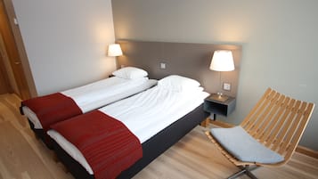 A double bed with white and red bedding, two bedside tables with lamps, a wooden chair, and a wooden floor.