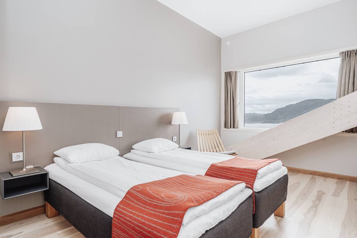 Habitación de hotel moderna con dos camas, un escritorio y una ventana con vistas a una montaña.
