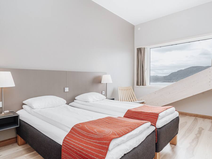 Quarto de hotel moderno com duas camas, uma escrivaninha e uma janela com vista para uma montanha.