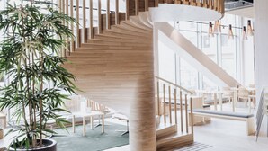 Et moderne interiør med en trappe i træ i spiralform, en stor potteplante og en siddeplads med borde og stole.