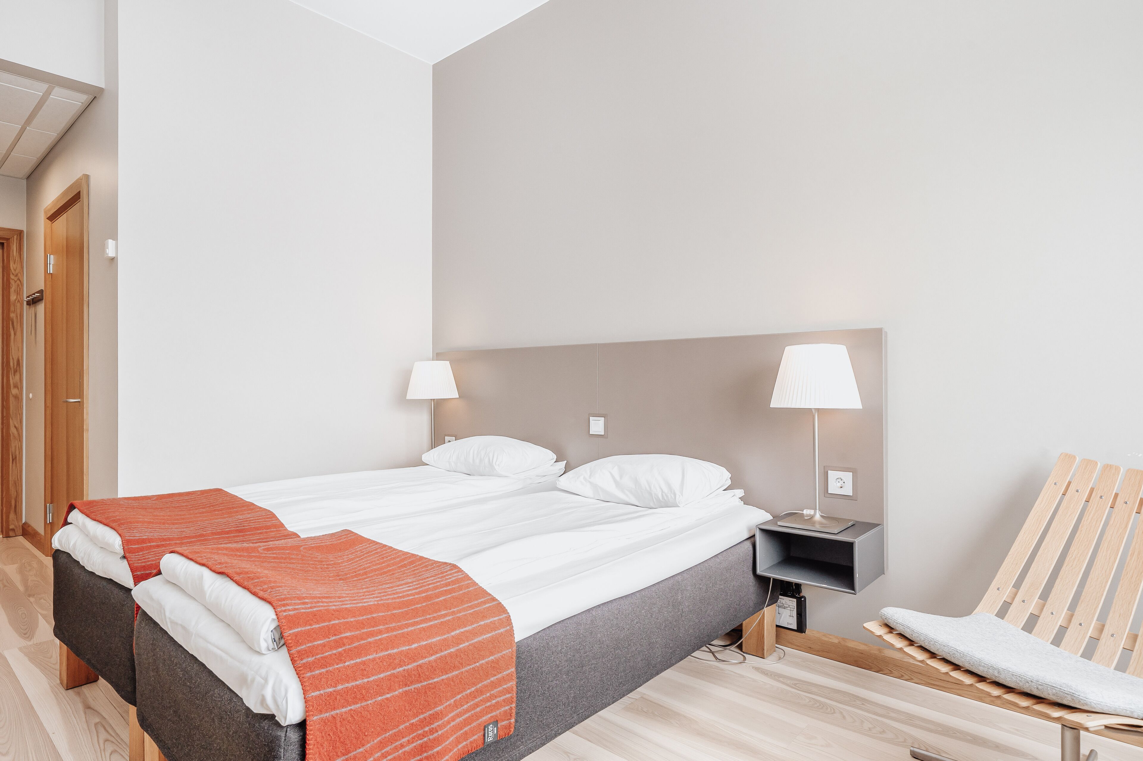 A modern hotel room with a bed, two bedside tables, a chair, and a lamp.