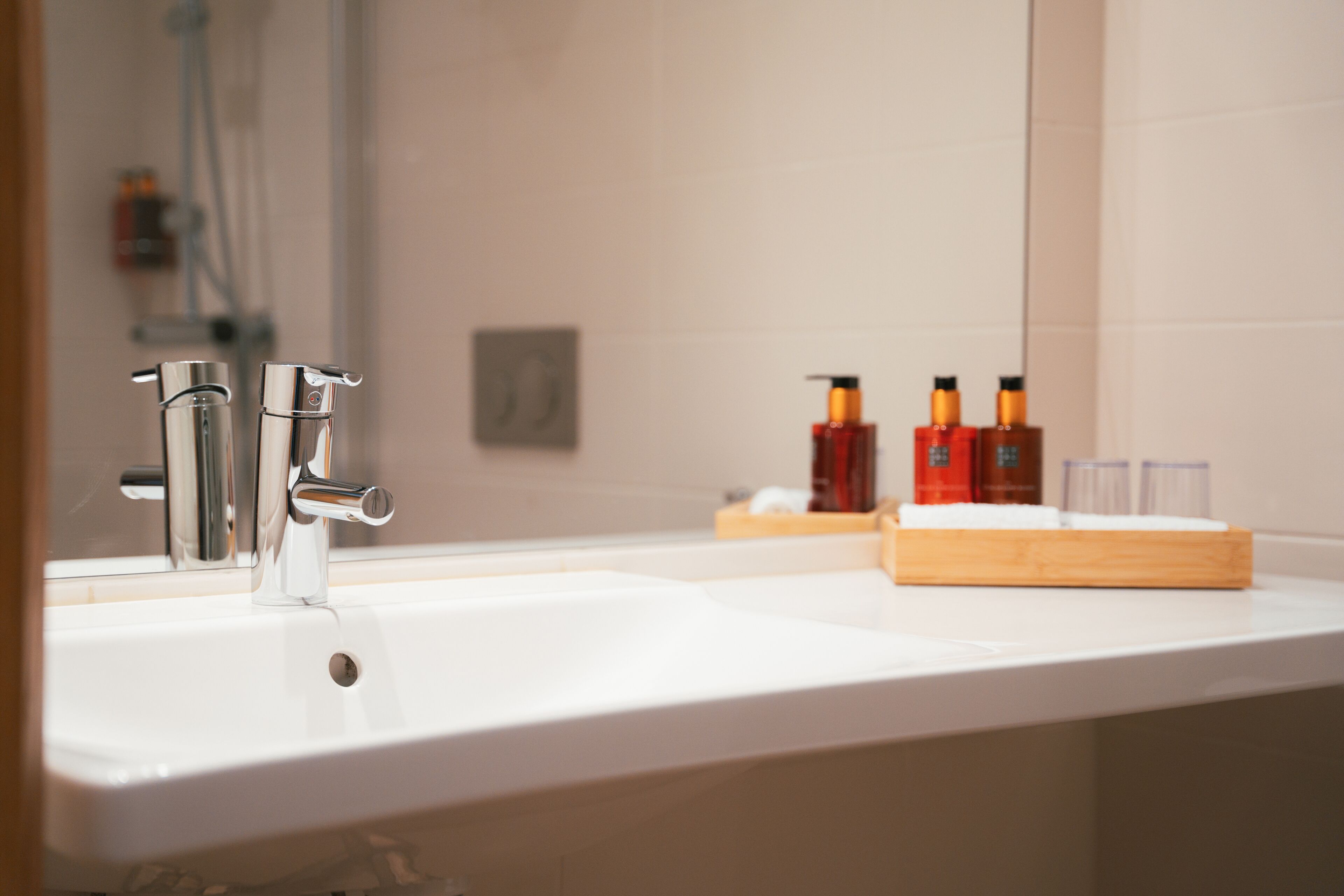 Un baño con lavamanos blanco, grifo cromado y espejo que refleja artículos de tocador.