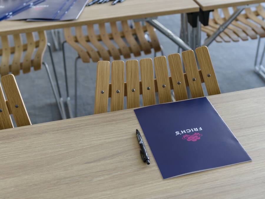 Un'aula con banchi e sedie di legno, un portatile e un quaderno su una scrivania.