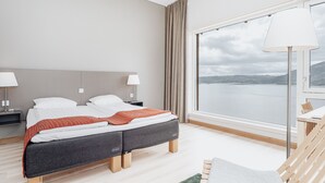 Et moderne soveværelse med en stor seng, et natbord, en lampe og udsigt til en sø gennem et stort vindue.
