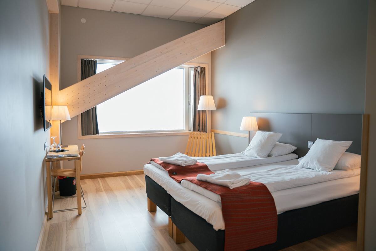 Una habitación de hotel moderna con una cama, dos mesitas de noche, un escritorio y una ventana con cortinas.