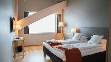 A modern hotel room with a bed, two bedside tables, a desk, and a window with curtains.