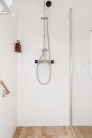 Un baño moderno con cabina de ducha de vidrio, cabezal de ducha manual y grifo empotrado.