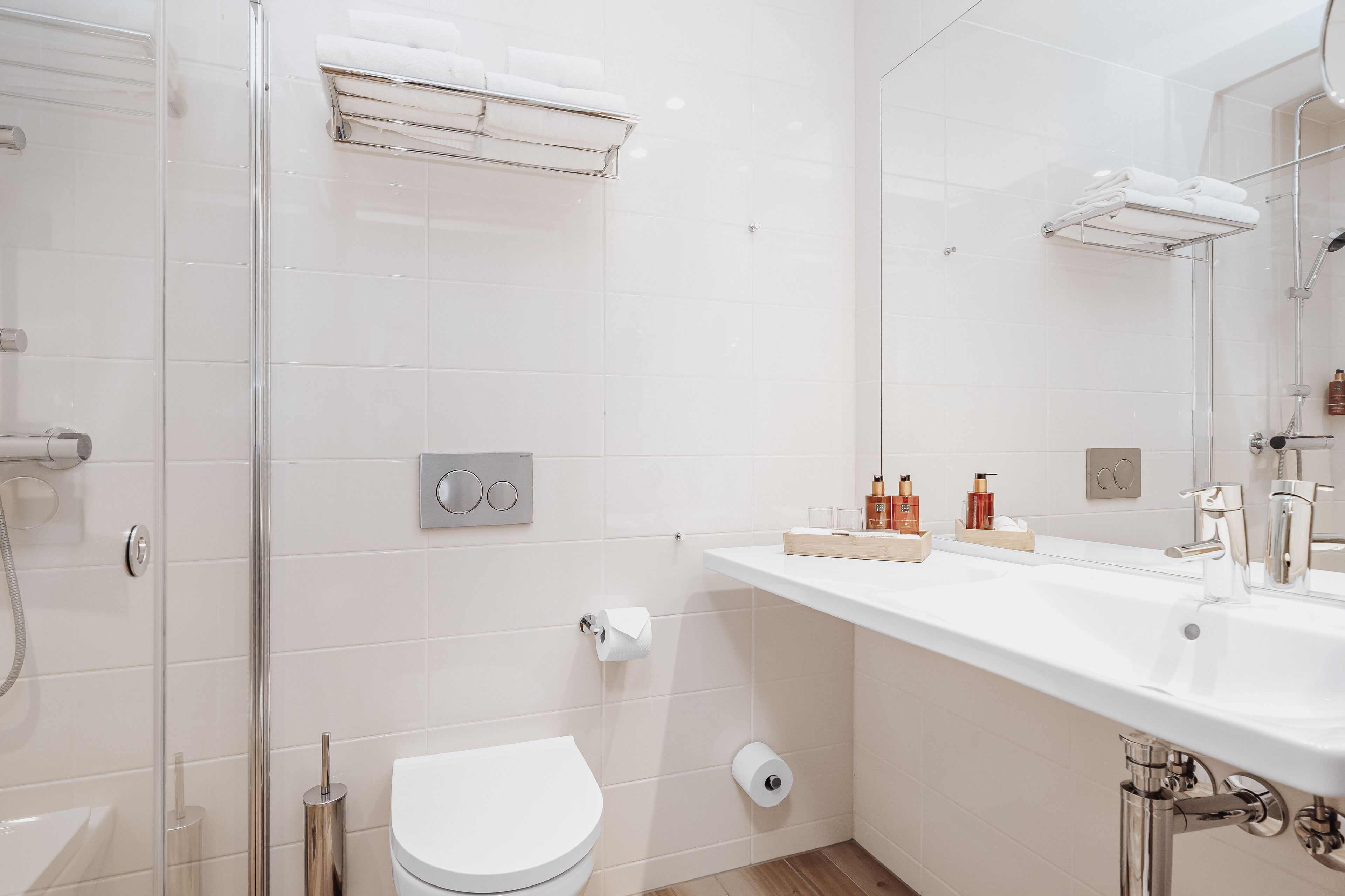 Un baño moderno con cabina de ducha de vidrio, un inodoro blanco, un lavamanos con espejo y artículos de aseo en la encimera.
