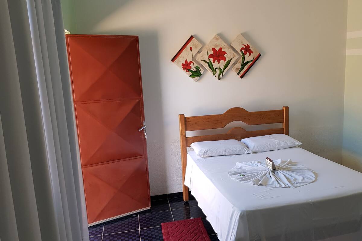 Un lit bien fait, avec du linge de lit blanc et une serviette, une tête de lit en bois et une armoire rouge.