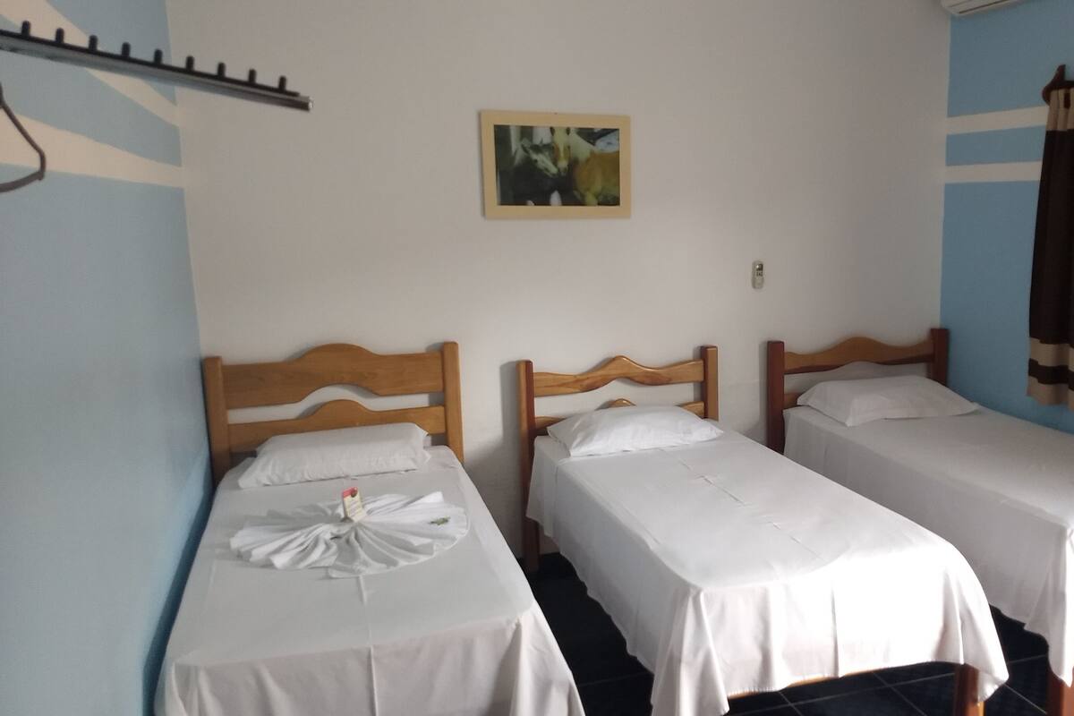 Une chambre avec deux lits simples, un petit tableau encadré accroché au mur et un rideau à la fenêtre.