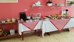Ein Frühstücksbuffet mit verschiedenen Speisen und Getränken, einer Mikrowelle und einer Kaffeemaschine auf einem Tisch mit rot-weißer Karotischdecke.