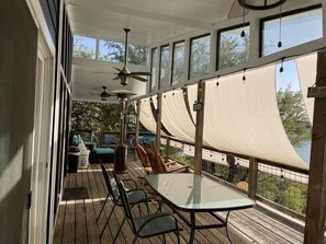 Un espacio al aire libre techado con una mesa, sillas y un ventilador de techo, con vista a una masa de agua.