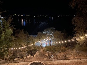 Un espacio al aire libre de noche con luces colgantes, árboles y terreno rocoso.