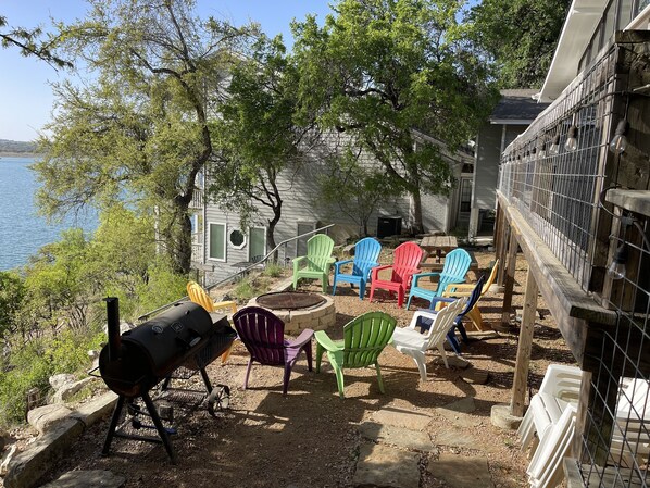 Un patio trasero con una parrilla, sillas Adirondack de colores y vistas a un lago.