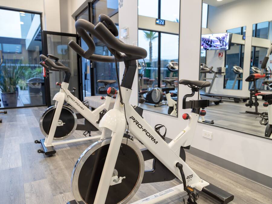 Una bicicleta estática en un gimnasio, con un espejo y equipo de ejercicio al fondo.