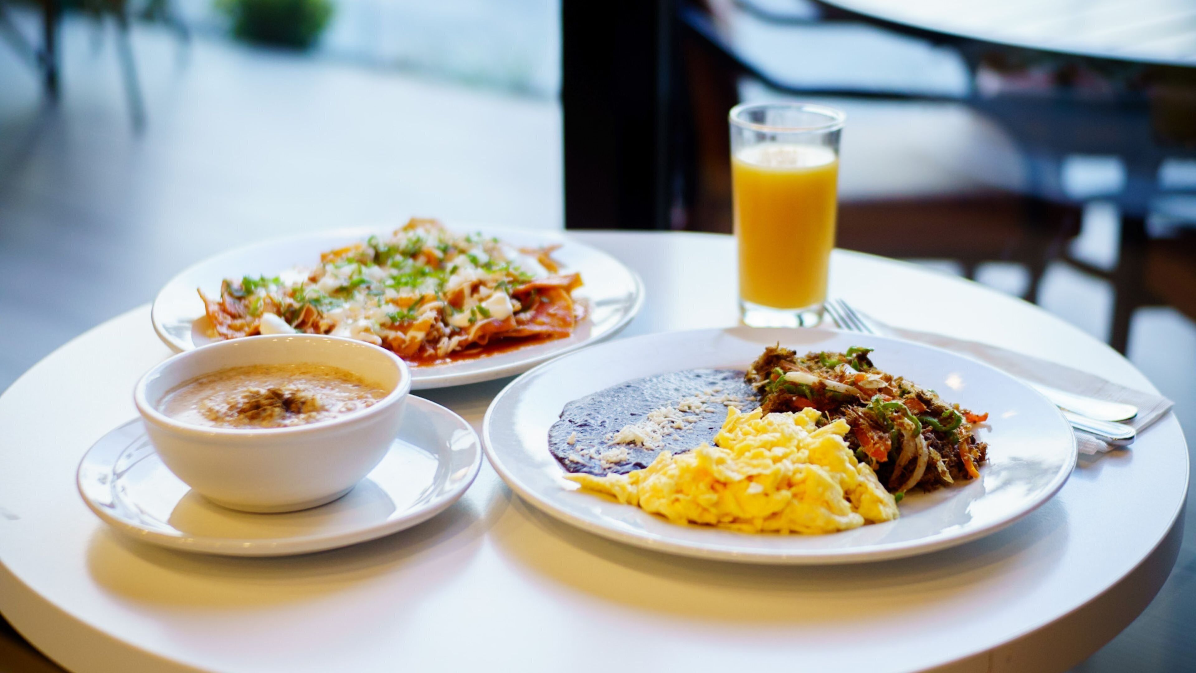 A table with two plates of food, a bowl of soup, and a glass of orange juice.