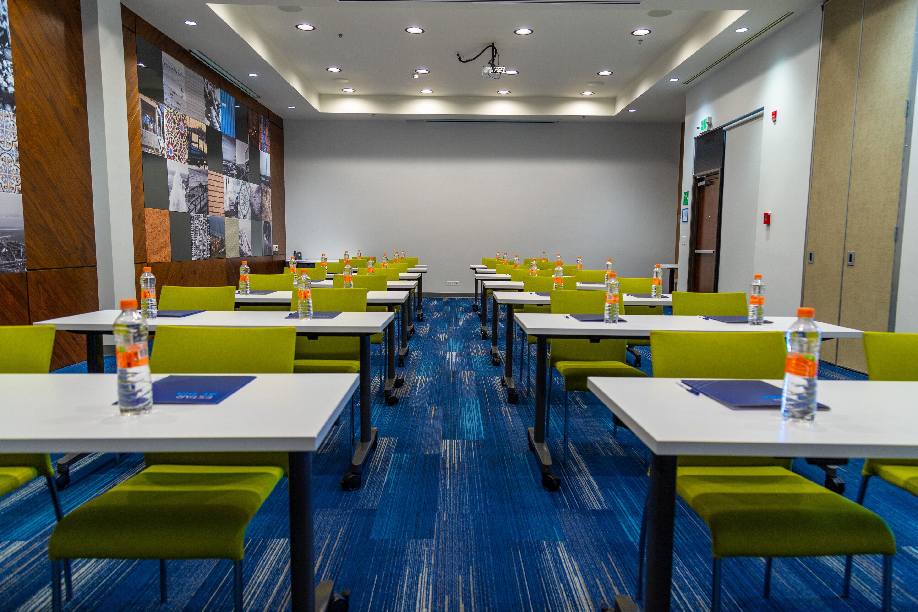 Un salón de conferencias con mesas y sillas, equipado con botellas de agua y un proyector.