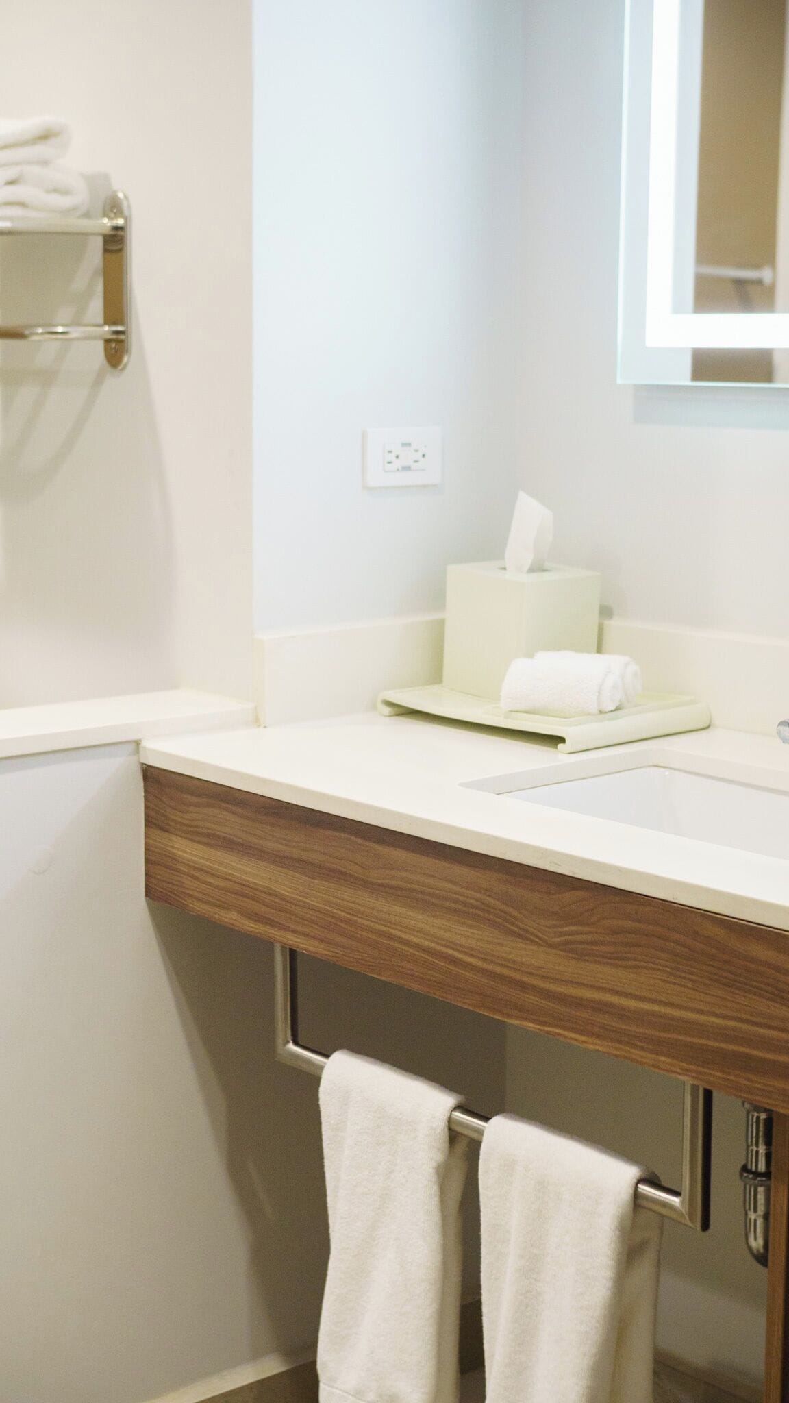 A bathroom with a wooden vanity, a mirror, a towel rack, and a tissue box.