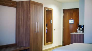 A hotel room with a large wardrobe, a mirror, a coffee station, and a bed.