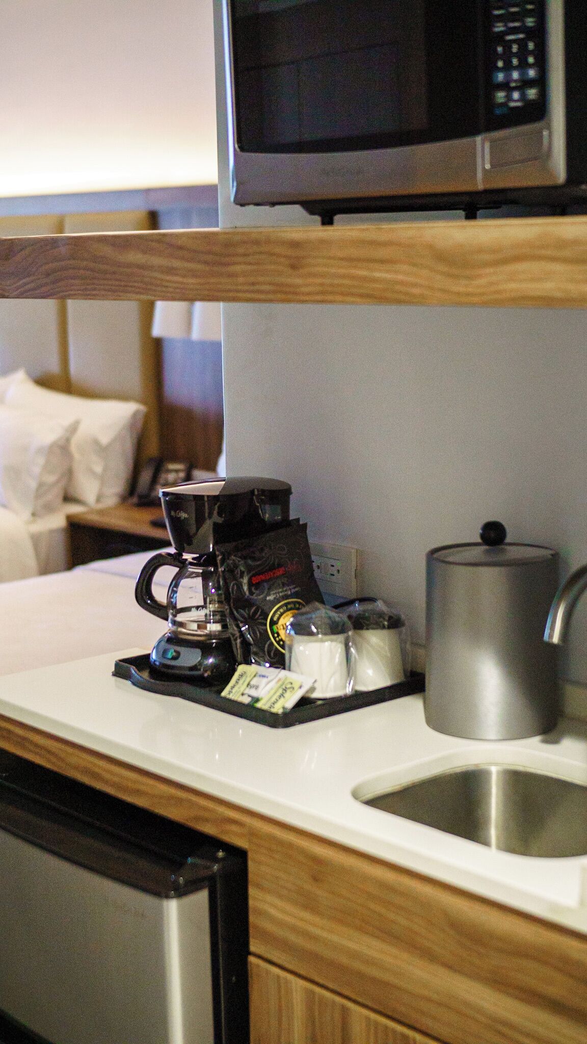Une petite cuisine équipée d’une machine à café, d’une bouilloire et d’un four à micro-ondes, le tout installé au-dessus de l’évier.