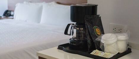 A coffee maker, a bag of coffee, and two containers on a hotel room's bedside table.