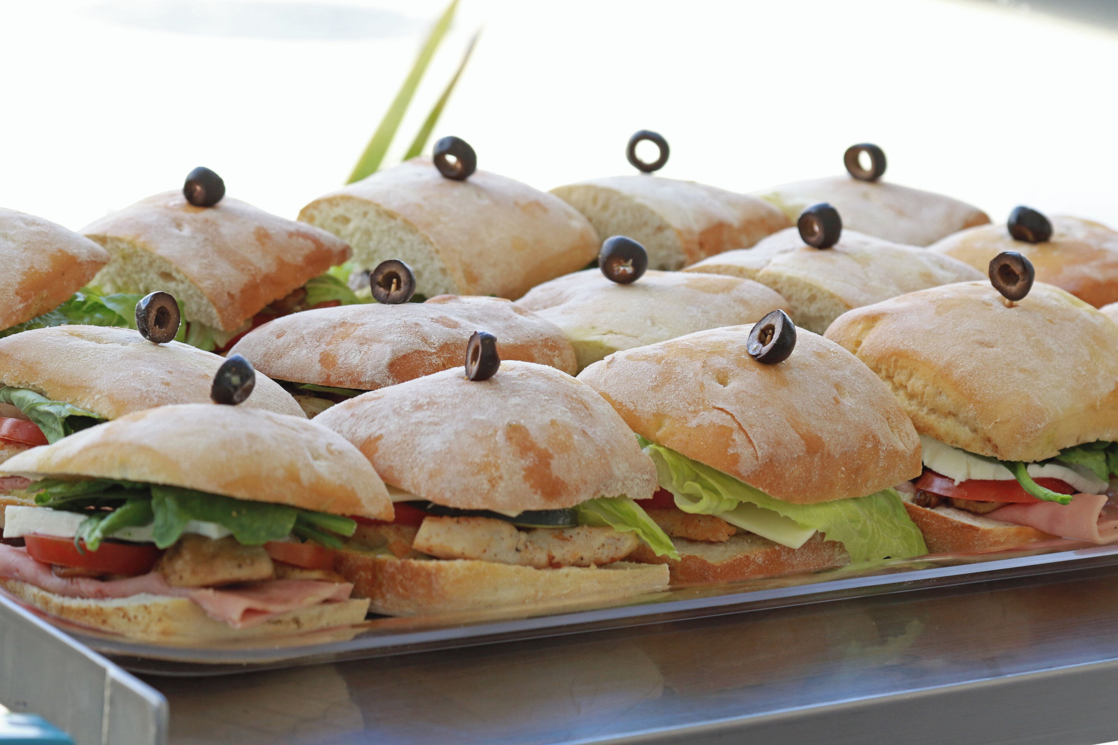 A tray of sandwiches with olives on top, arranged on a metal surface.