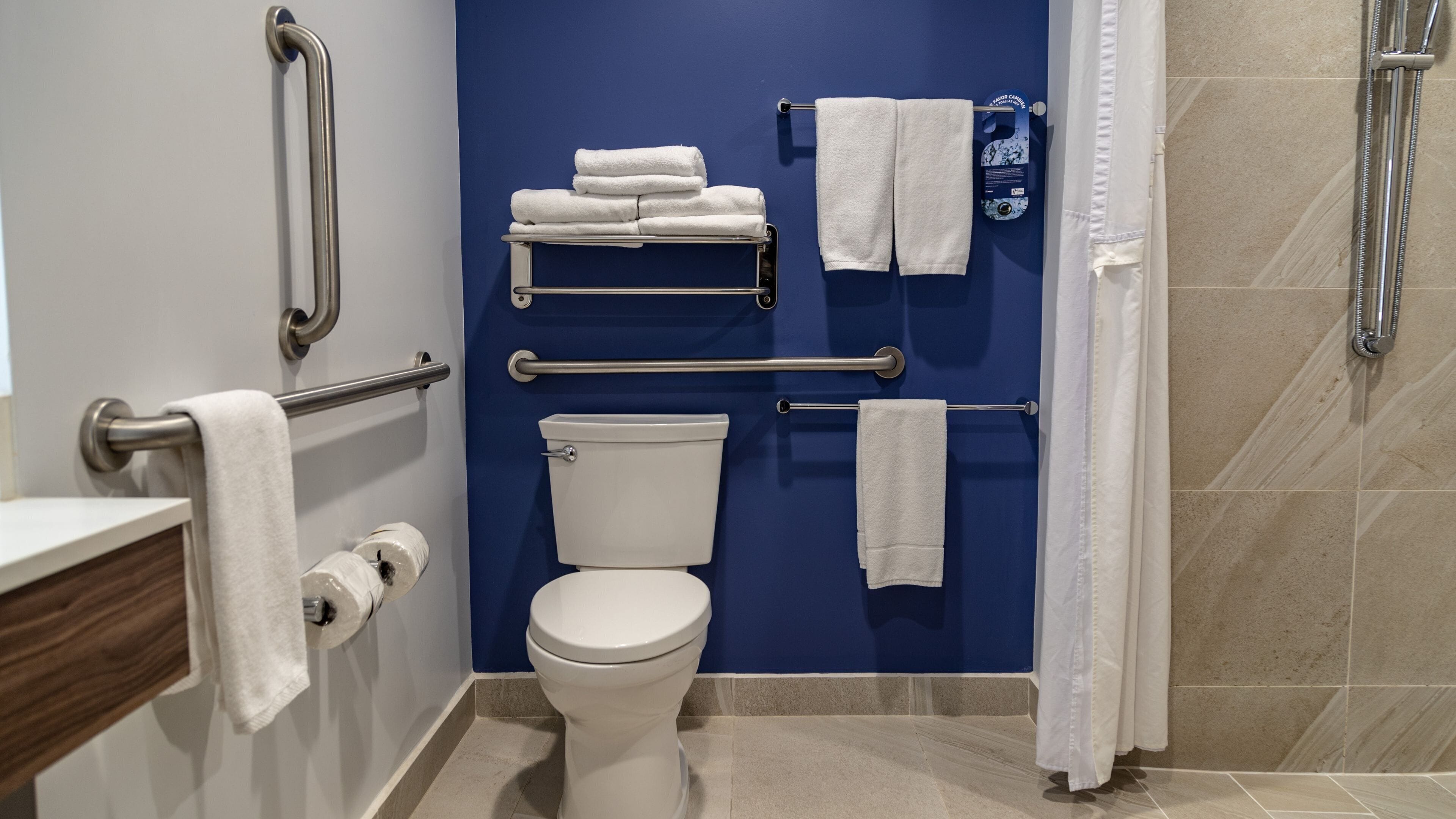 Un baño con pared azul, inodoro blanco, ducha con cortina y varios toalleros.