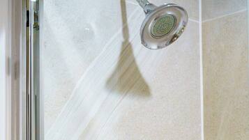 A shower area with a handheld showerhead, a glass door, and two Dove body wash bottles on a wall-mounted holder.