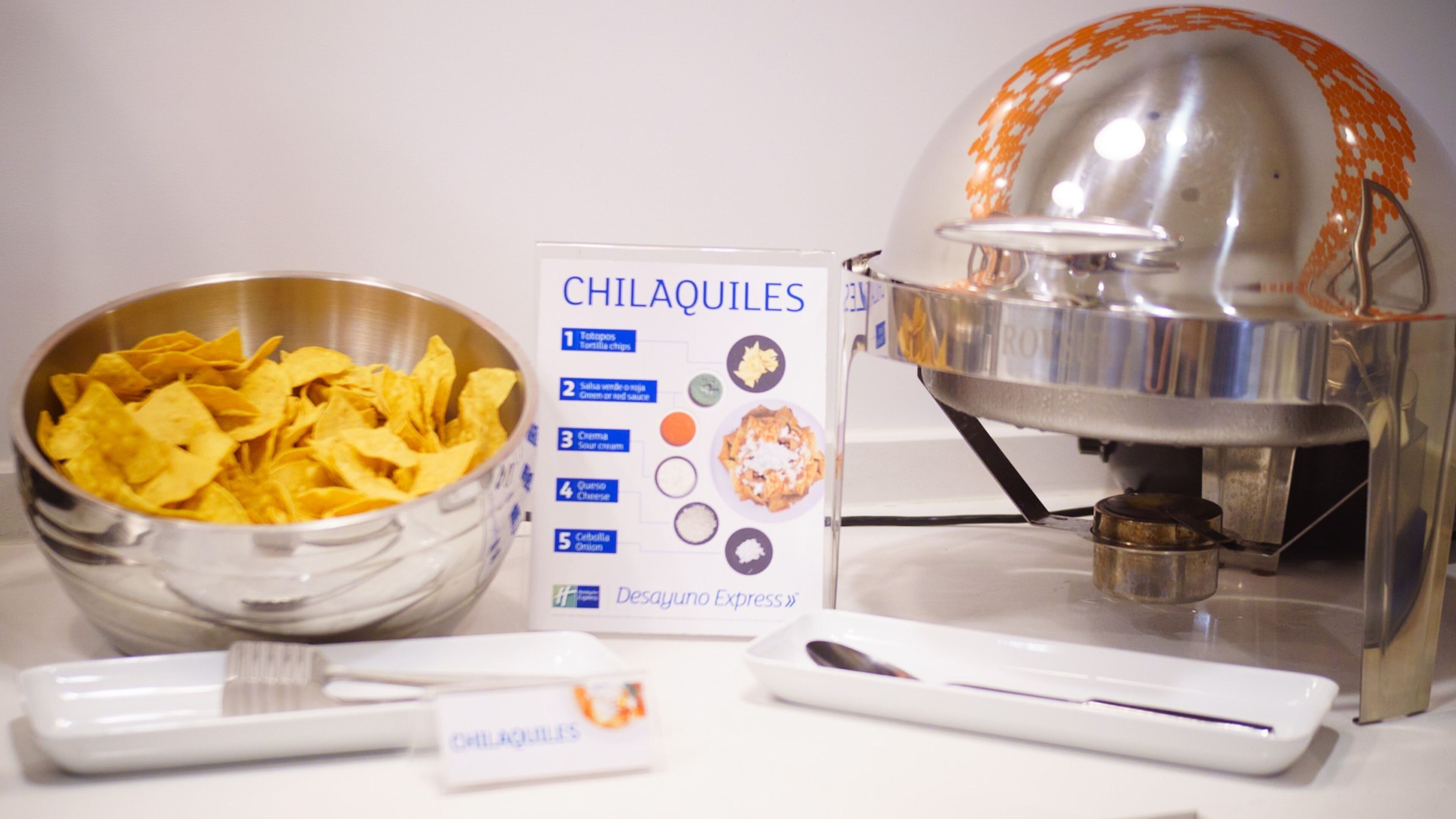 Een voorbereidingsruimte voor voedsel met een schaal chips, een voedingsschema, een keukenmachine en een naambordje.