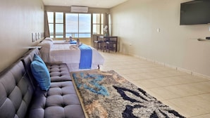 A hotel room with a large window, a flat-screen TV, a sofa, a bed, and a small table. - Oceanfront Resort Studio - 2 Mi to Rincon Plaza! (Rincon)