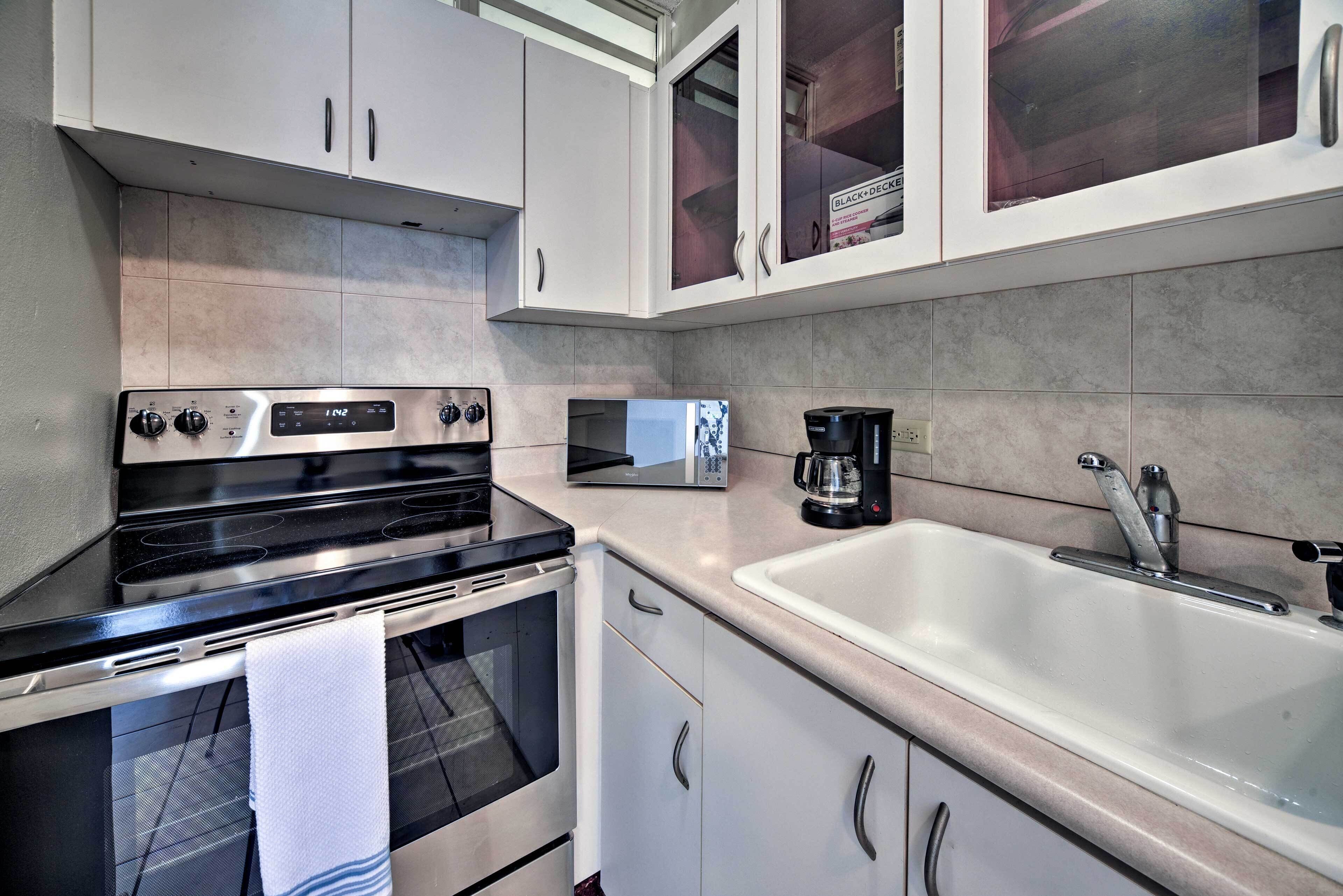 A modern kitchen with white cabinets, a stainless steel stove, a microwave, and a sink.