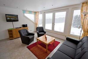 A living room with a sofa, two armchairs, a coffee table, a TV, and a window with a view of a snowy landscape.
