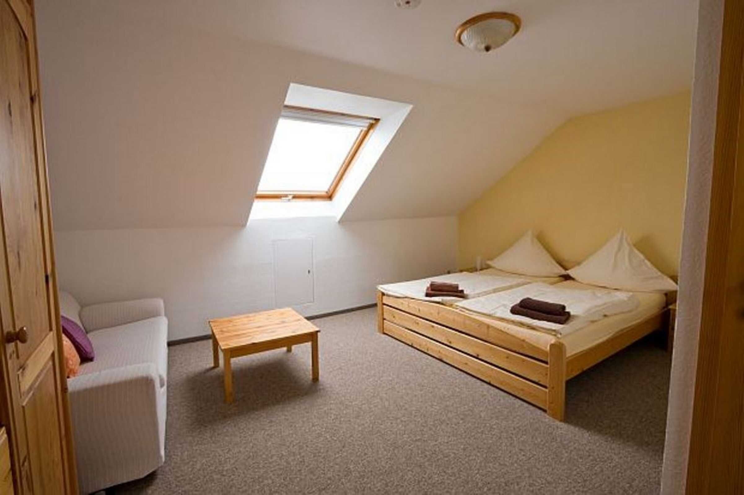 Un petit appartement d’une seule pièce, avec un plafond en pente, un puits de lumière, un lit, une chaise et une petite table.