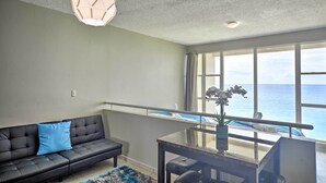 A modern living room with a black leather sofa, a glass coffee table, and a view of the ocean through large windows. - Rincon Penthouse: Steps to Private Beach Oasis! (Rincon)