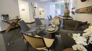 Un hall d’hôtel moderne comprenant un espace salon, un coin café et un vase décoratif orné d’orchidées.