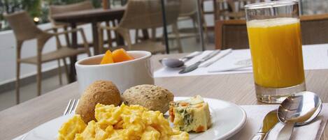 A breakfast setting with scrambled eggs, muffins, and a glass of orange juice on a table with a view of the outdoors.