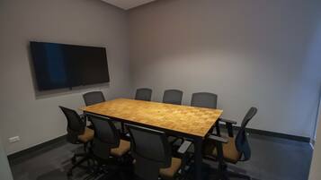 Una sala de conferencias con una mesa grande, ocho sillas y un televisor de pantalla plana montado en la pared.
