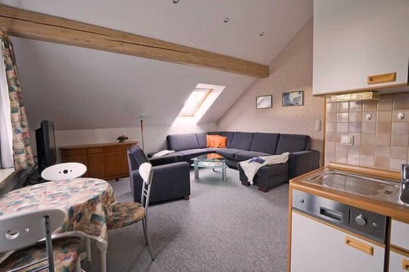 A compact living space with a kitchenette, a sofa, a dining table, and a small TV.