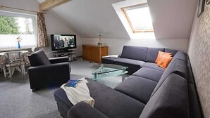 Un salon moderne avec un canapé, un fauteuil, une table basse en verre, un téléviseur et une fenêtre donnant sur un beau paysage.