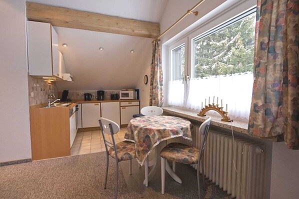 A compact kitchen with a dining area, a window with curtains, and a radiator.