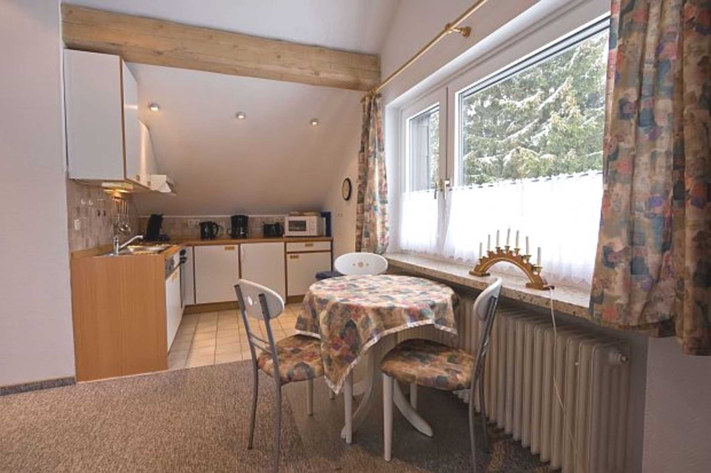 A compact kitchen with a dining area, a window with curtains, and a radiator.