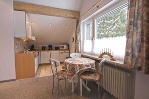 Une cuisine de taille réduite avec un coin repas, une fenêtre avec des rideaux et un radiateur.