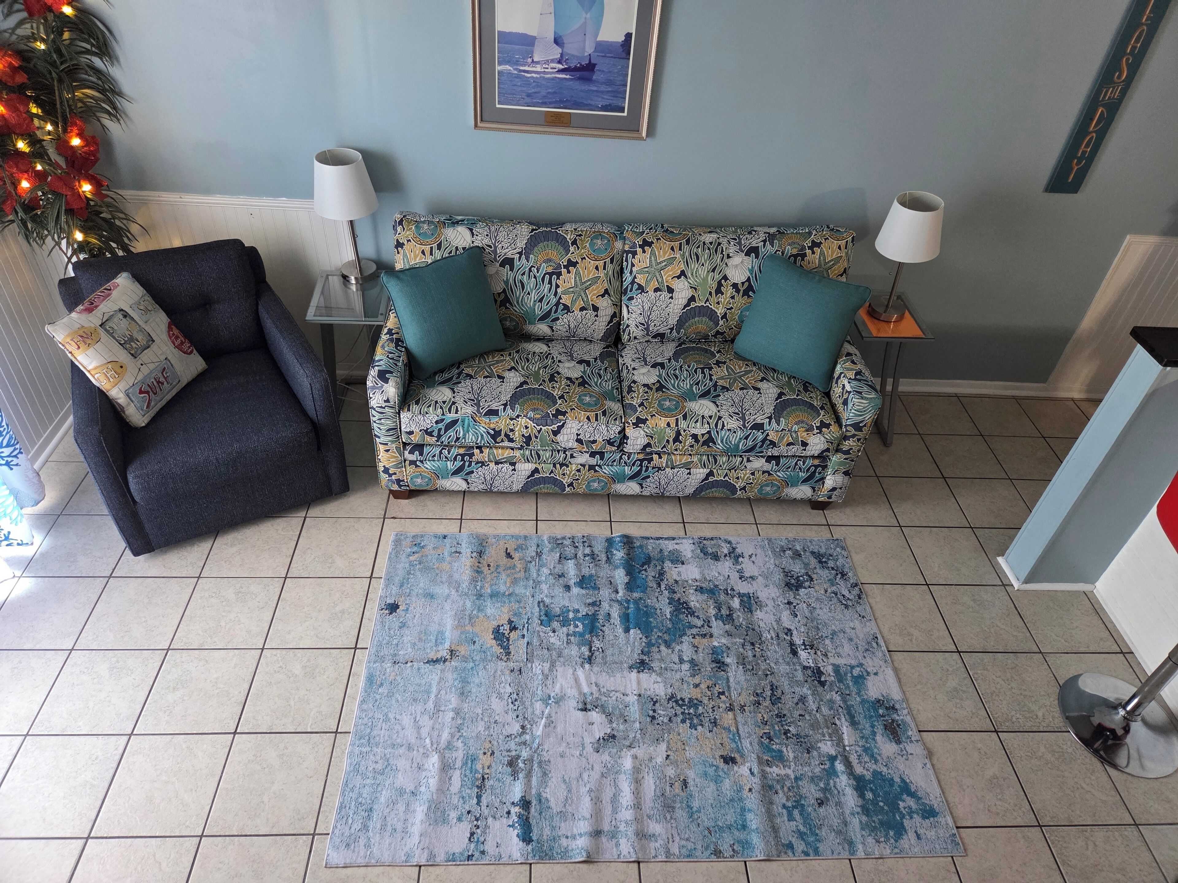 A living room with a patterned sofa, a small armchair, a blue rug, and a framed picture on the wall.