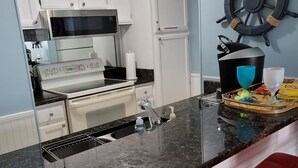 Een keuken met witte kastjes, een zwart-wit fornuis, een spoelbak met zeepdispenser en een decoratie van een scheepsschroef.
