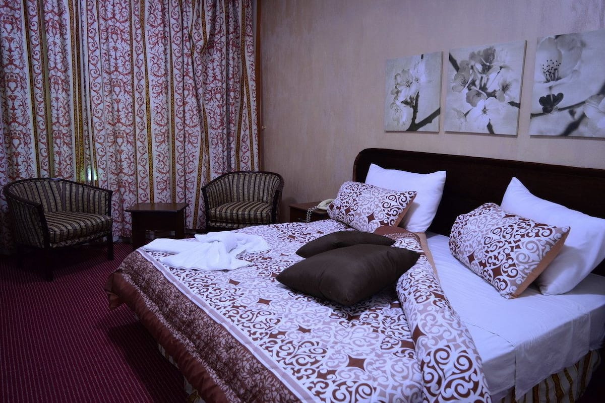 A hotel room with a large bed, two chairs, a small table, and floral artwork on the wall.