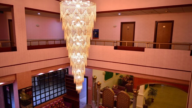 En hotellobby med en stor kristallkrona, en sittgrupp med mönstrade soffor och en trappa som leder upp till en våning ovanför.