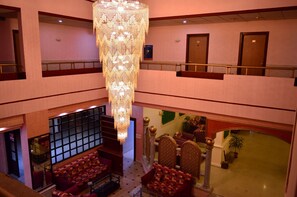 Un hall d’hôtel doté d’un grand lustre, d’un espace salon avec des canapés à motifs et d’un escalier menant à l’étage supérieur.