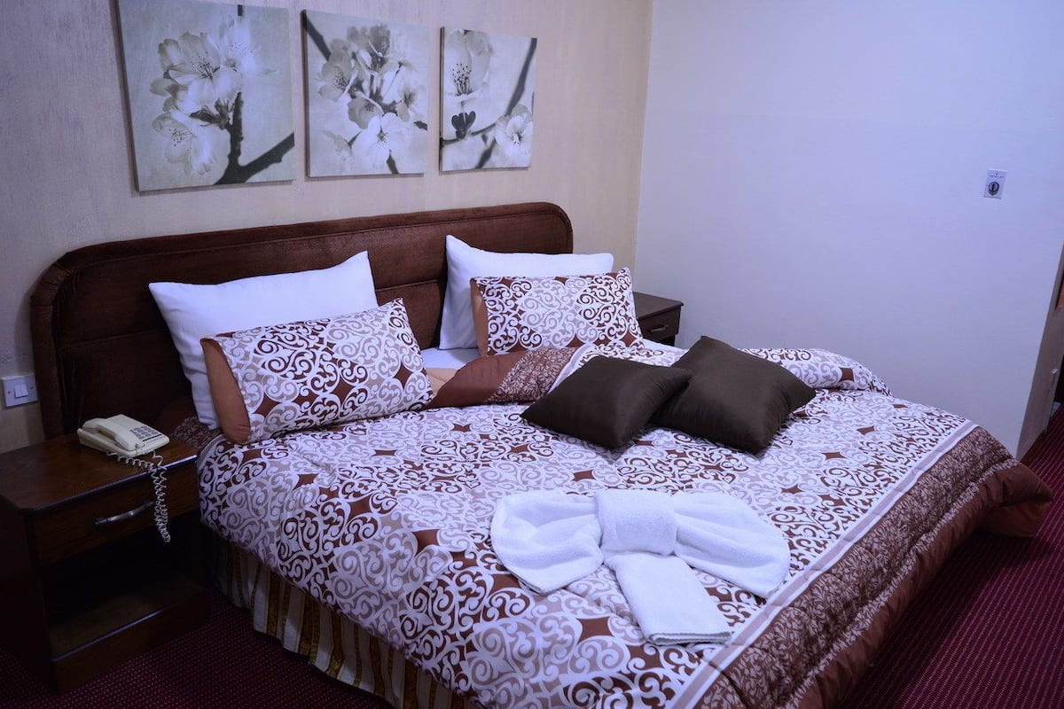 A neatly made bed with patterned bedding, a bedside table with a phone, and wall art above the bed.